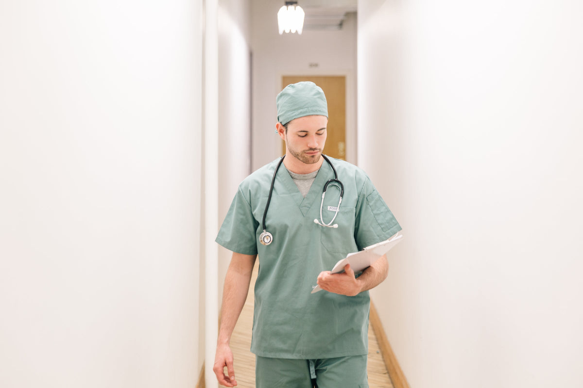 Nurse in scrubs walking down a hospital hallway reading a clipboard
